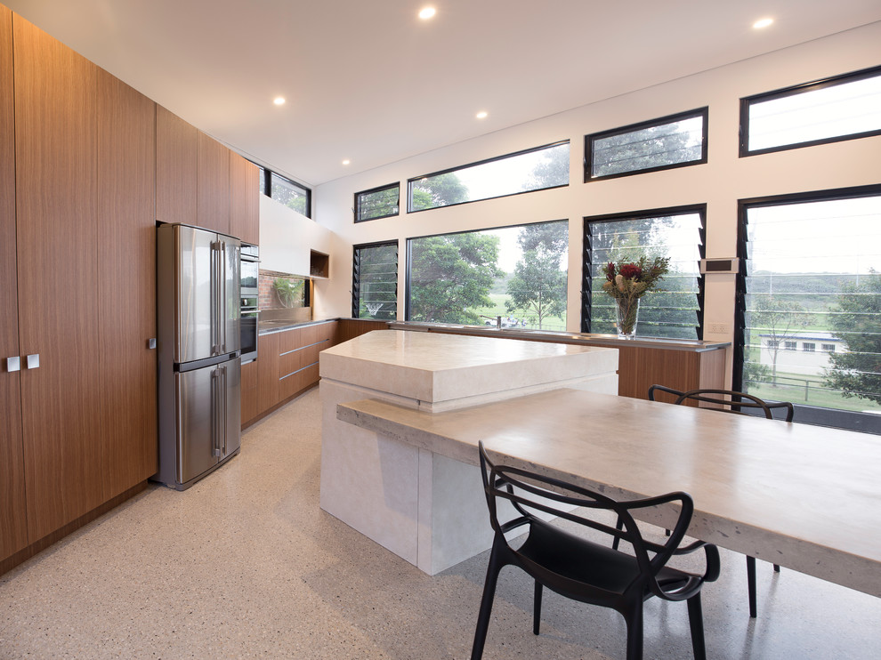 Modern inredning av ett stort kök, med släta luckor, skåp i mellenmörkt trä, bänkskiva i rostfritt stål, glaspanel som stänkskydd, rostfria vitvaror, betonggolv och en köksö