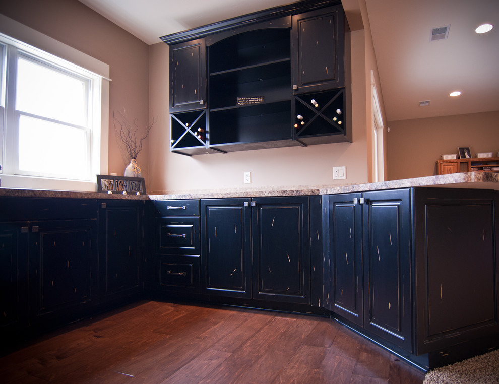 Klassisk inredning av ett litet brun brunt kök, med en nedsänkt diskho, luckor med profilerade fronter, svarta skåp, granitbänkskiva, rostfria vitvaror, mellanmörkt trägolv, en halv köksö och brunt golv