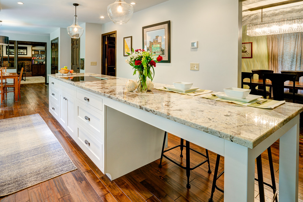 Example of a mid-sized transitional galley medium tone wood floor eat-in kitchen design in Columbus with an island, shaker cabinets, white cabinets, granite countertops, white backsplash, subway tile backsplash, stainless steel appliances and a double-bowl sink