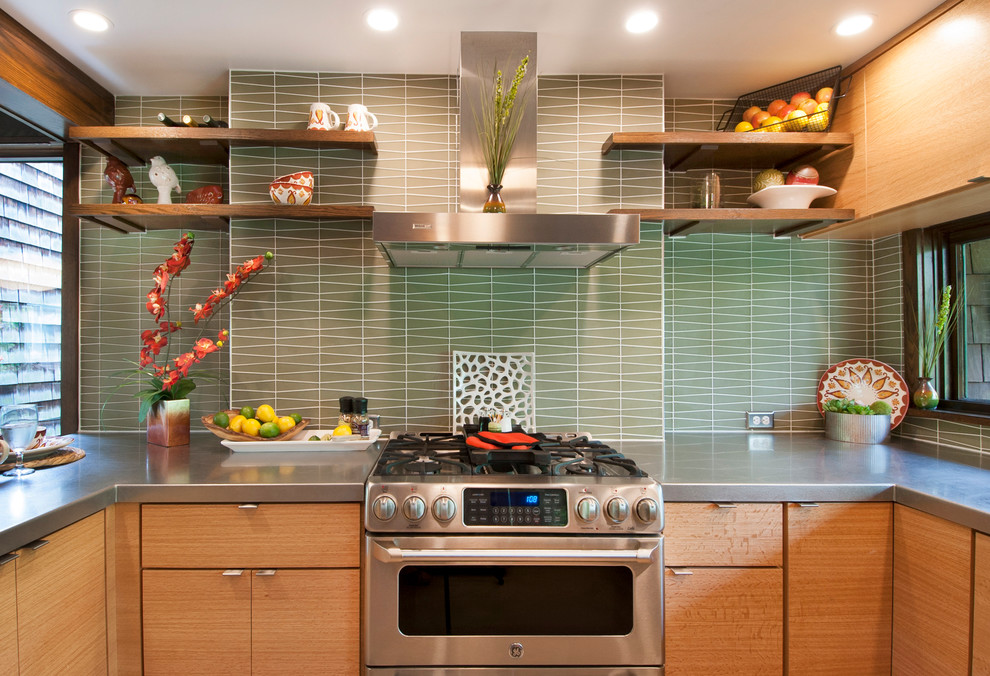 Cette photo montre une cuisine rétro en U et bois clair avec un placard à porte plane, un plan de travail en inox, une crédence verte, une crédence en carreau de verre et un électroménager en acier inoxydable.