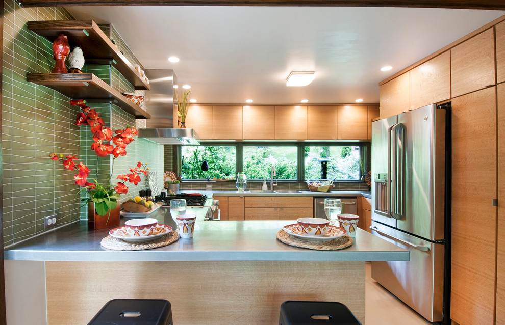 Immagine di una piccola cucina moderna con lavello integrato, ante lisce, ante in legno chiaro, top in acciaio inossidabile, paraspruzzi verde, paraspruzzi con piastrelle di vetro, elettrodomestici in acciaio inossidabile, pavimento in linoleum e penisola