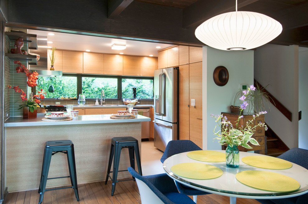 This is an example of a small midcentury u-shaped open plan kitchen in Columbus with an integrated sink, flat-panel cabinets, light wood cabinets, stainless steel worktops, green splashback, glass tiled splashback, stainless steel appliances, lino flooring and a breakfast bar.