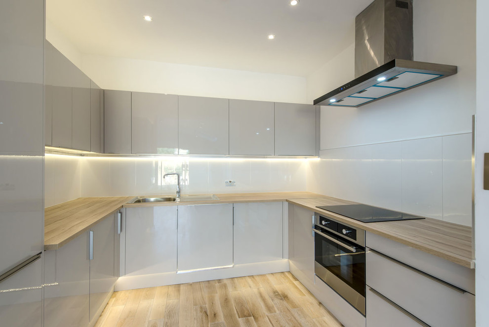 Design ideas for a medium sized modern u-shaped enclosed kitchen in London with a built-in sink, flat-panel cabinets, grey cabinets, wood worktops, white splashback, glass sheet splashback, stainless steel appliances, plywood flooring, no island, multi-coloured floors and multicoloured worktops.