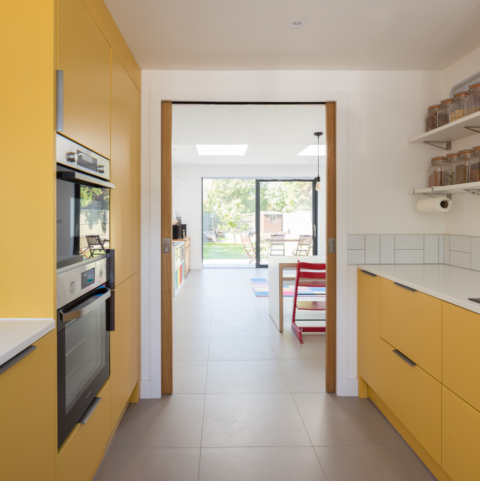 Design ideas for a small contemporary u-shaped enclosed kitchen in Cambridgeshire with flat-panel cabinets, yellow cabinets, composite countertops, white splashback, ceramic splashback, stainless steel appliances, ceramic flooring, grey floors, white worktops and no island.