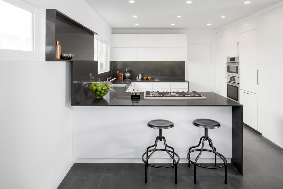 Inspiration for a contemporary u-shaped eat-in kitchen remodel in Los Angeles with flat-panel cabinets, white cabinets, paneled appliances, a peninsula, quartz countertops, black backsplash and an undermount sink