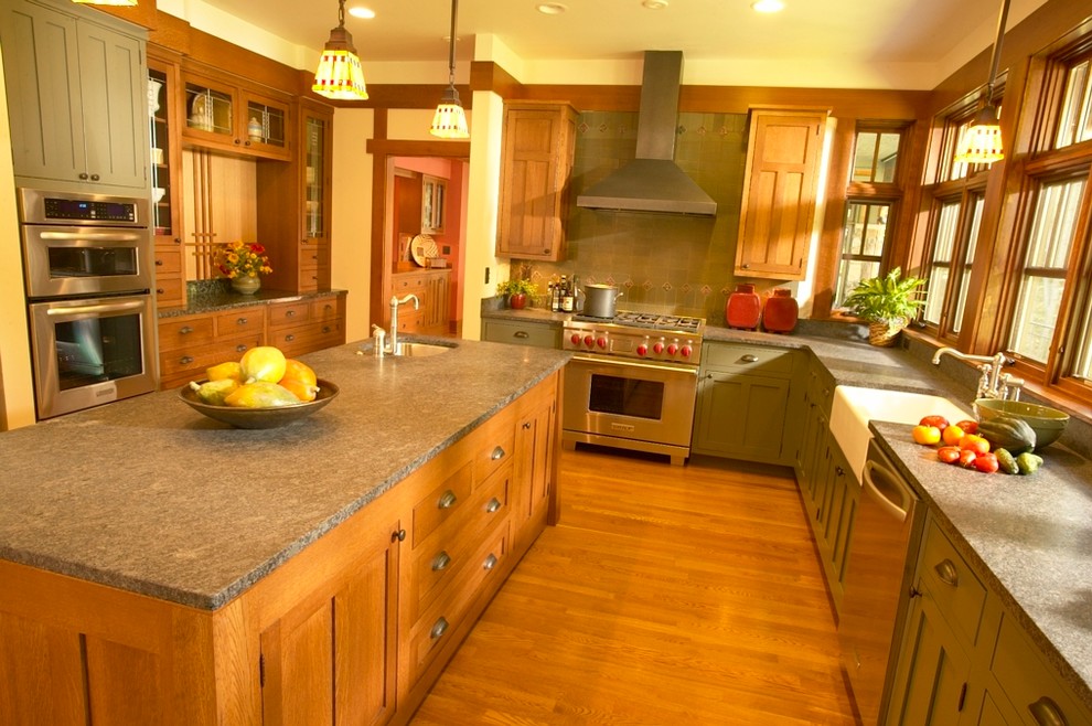 Cette image montre une cuisine craftsman avec un évier de ferme, un placard à porte plane, des portes de placards vertess, une crédence grise et un électroménager en acier inoxydable.