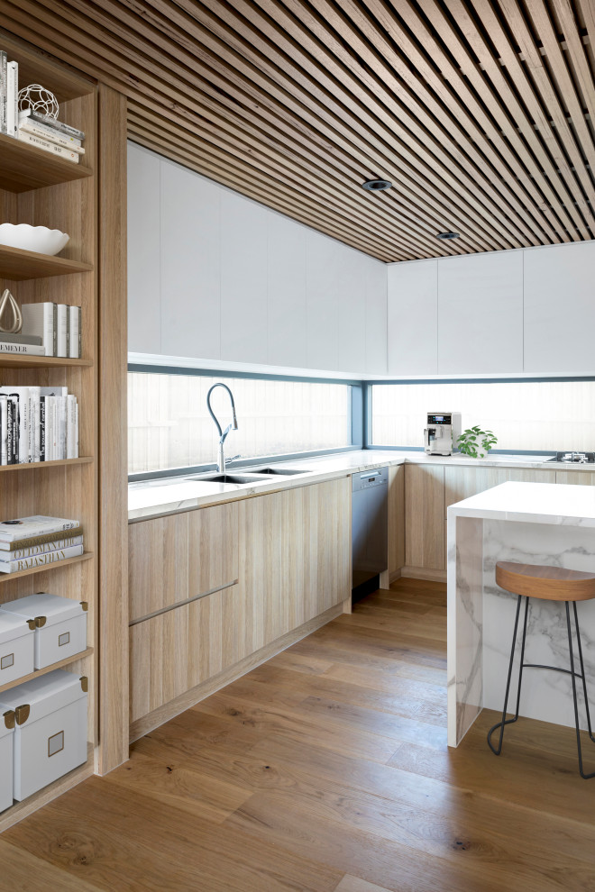 Inspiration för stora moderna vitt kök, med en undermonterad diskho, släta luckor, skåp i ljust trä, marmorbänkskiva, fönster som stänkskydd, svarta vitvaror, ljust trägolv, en köksö och brunt golv