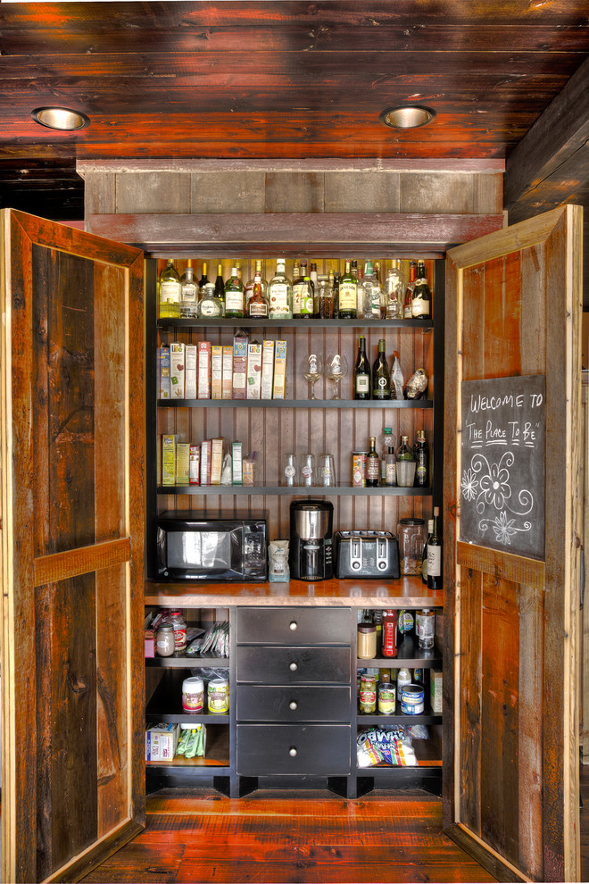 This is an example of a medium sized rustic galley kitchen pantry in Minneapolis with a belfast sink, wood worktops, stainless steel appliances, dark hardwood flooring, an island, shaker cabinets, red cabinets, brown splashback, wood splashback and brown floors.