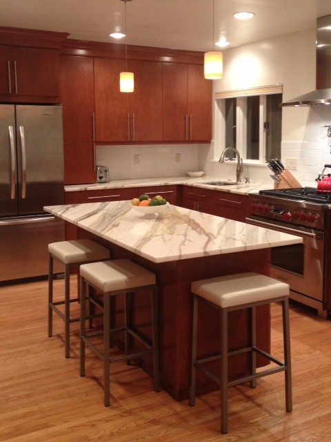 Modern inredning av ett mellanstort kök, med en undermonterad diskho, släta luckor, skåp i mellenmörkt trä, marmorbänkskiva, vitt stänkskydd, stänkskydd i keramik, rostfria vitvaror, ljust trägolv och en köksö