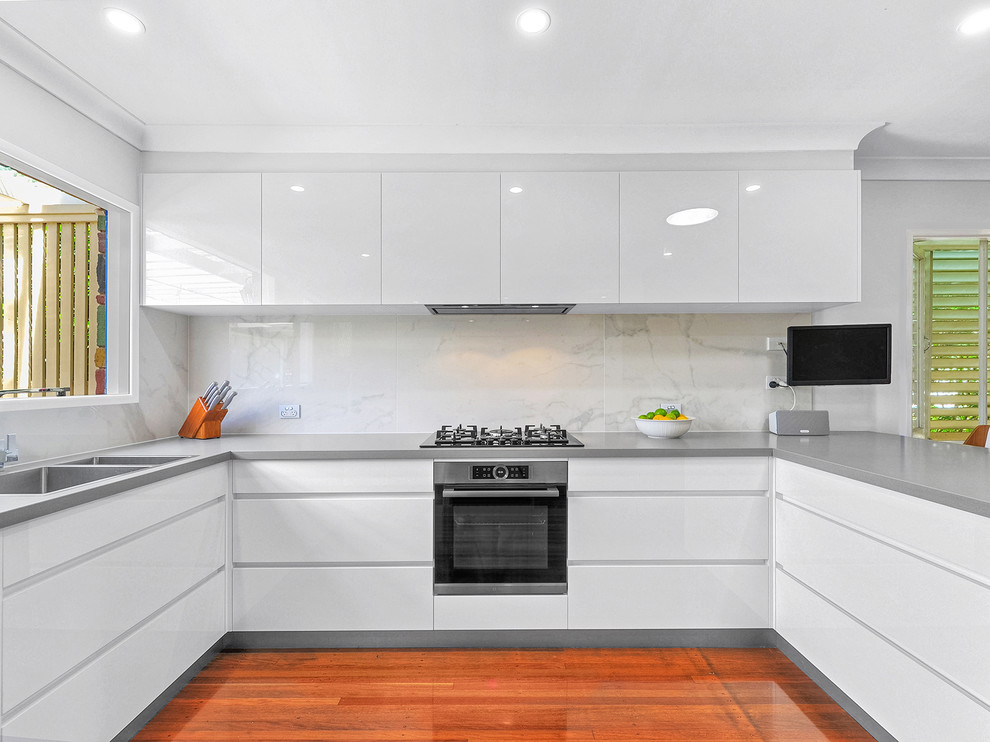 Mid-sized trendy u-shaped medium tone wood floor and orange floor open concept kitchen photo in Brisbane with a drop-in sink, flat-panel cabinets, white cabinets, quartz countertops, multicolored backsplash, porcelain backsplash, stainless steel appliances and a peninsula