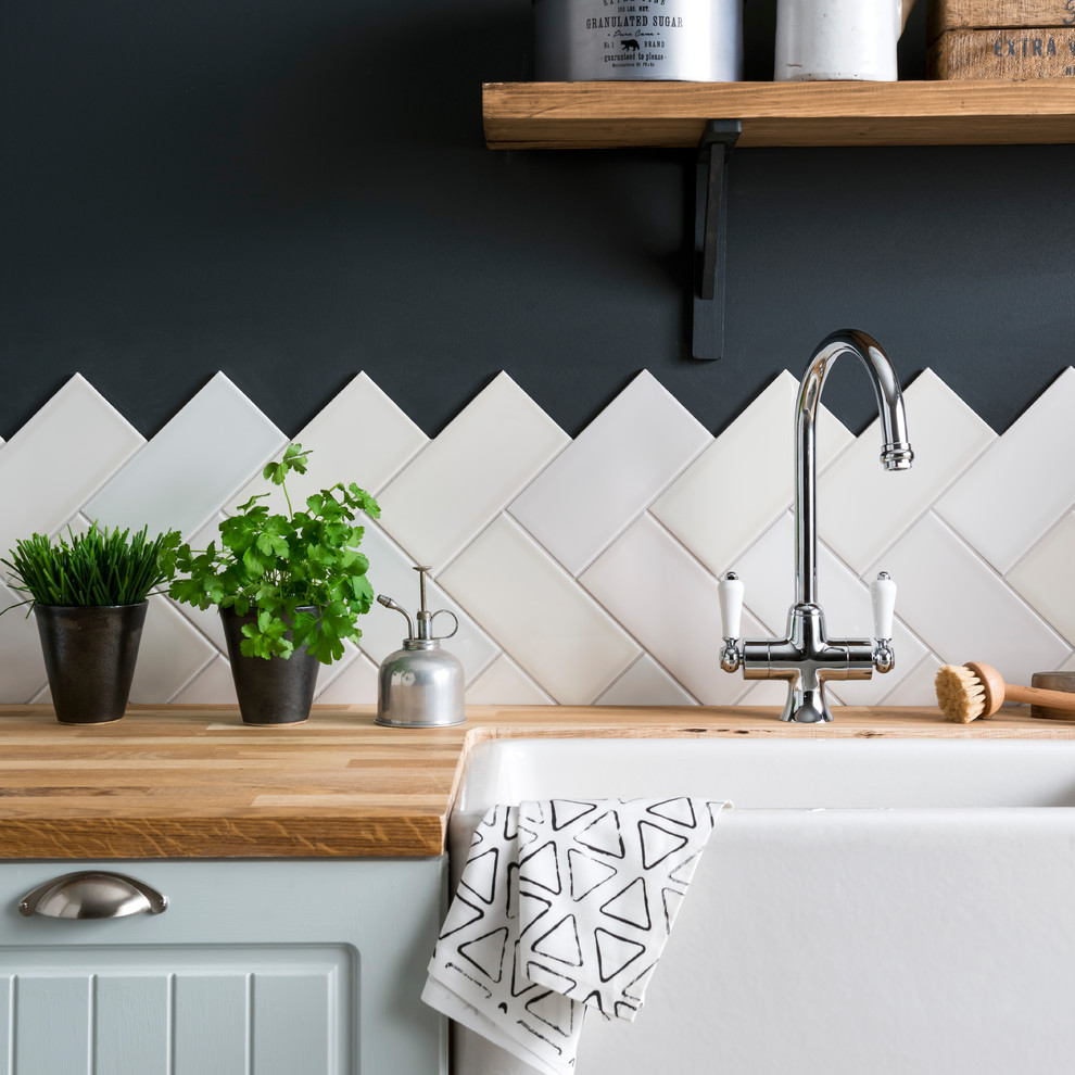 Example of a mid-sized trendy ceramic tile and black floor kitchen design in Other with a farmhouse sink, blue cabinets, wood countertops, white backsplash and ceramic backsplash