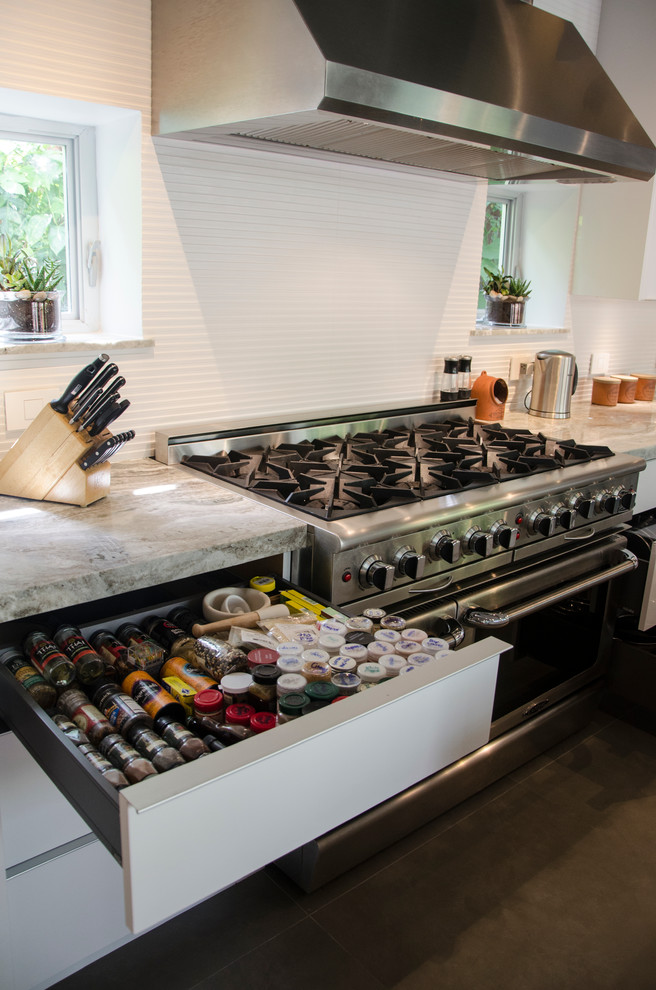 This is an example of a large contemporary single-wall open plan kitchen in Miami with a submerged sink, flat-panel cabinets, white cabinets, granite worktops, white splashback, porcelain splashback, stainless steel appliances, slate flooring and an island.