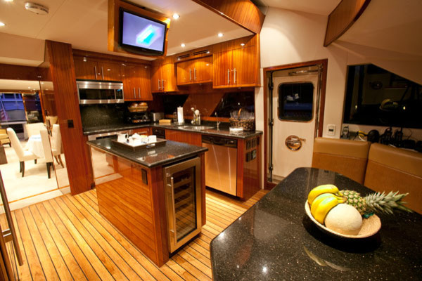Bild på ett mellanstort maritimt kök, med släta luckor, skåp i mellenmörkt trä, granitbänkskiva, rostfria vitvaror, ljust trägolv och en köksö