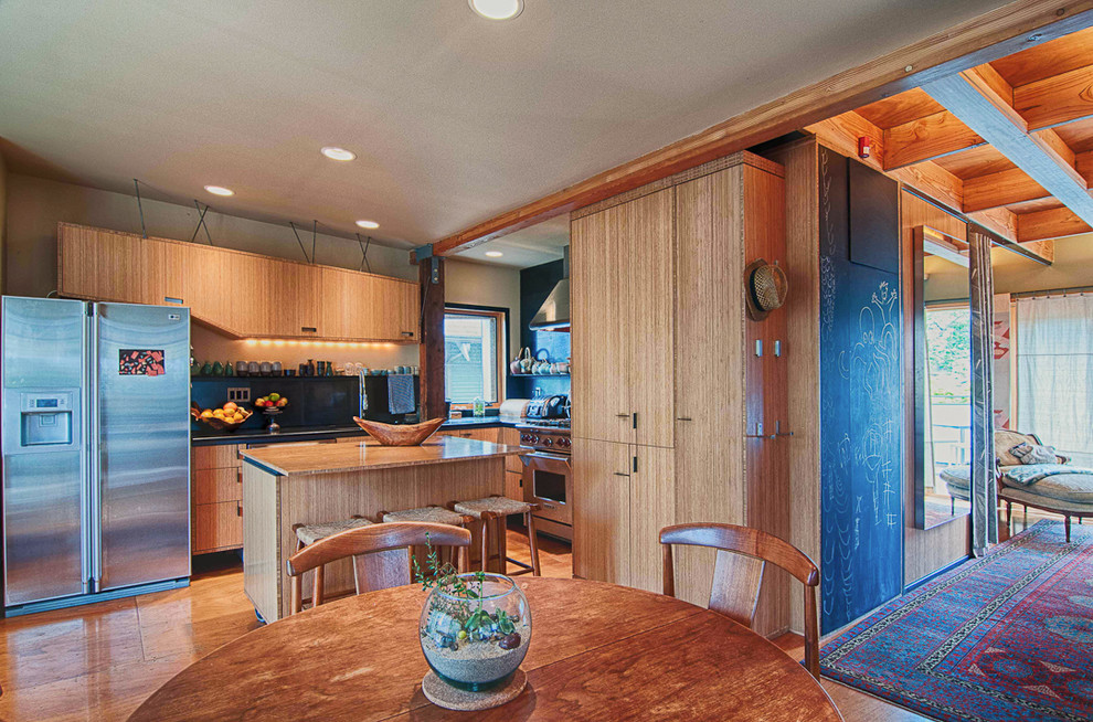 Diseño de cocina contemporánea con armarios con paneles lisos, puertas de armario de madera clara, salpicadero negro y electrodomésticos de acero inoxidable
