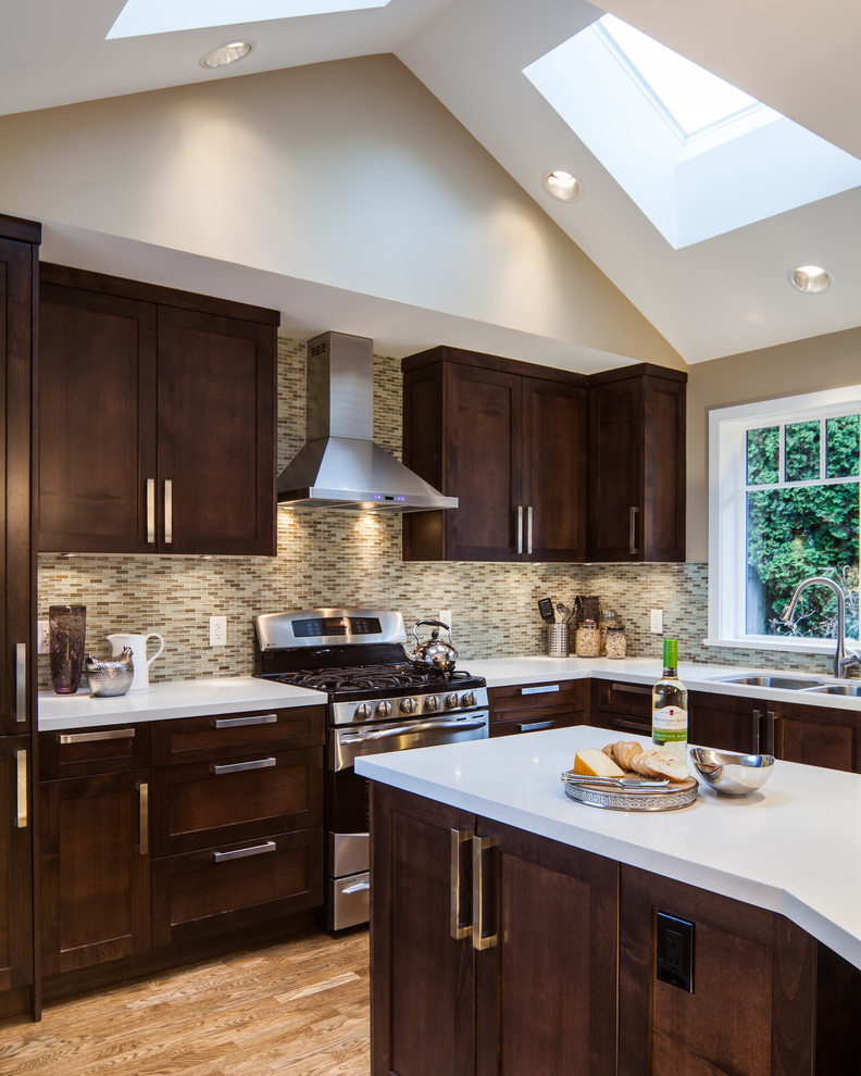 Example of a transitional l-shaped medium tone wood floor kitchen design in Vancouver with a double-bowl sink, shaker cabinets, dark wood cabinets, multicolored backsplash, mosaic tile backsplash and stainless steel appliances