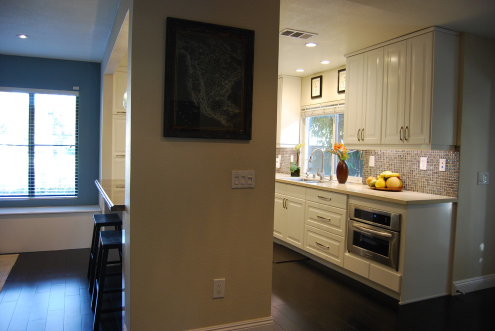 Foto på ett mellanstort funkis kök, med en undermonterad diskho, luckor med lamellpanel, vita skåp, granitbänkskiva, blått stänkskydd, rostfria vitvaror, mörkt trägolv och en köksö