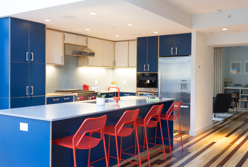 Example of a mid-sized trendy galley medium tone wood floor eat-in kitchen design in Vancouver with an undermount sink, flat-panel cabinets, blue cabinets, quartz countertops, green backsplash, glass tile backsplash, stainless steel appliances and an island