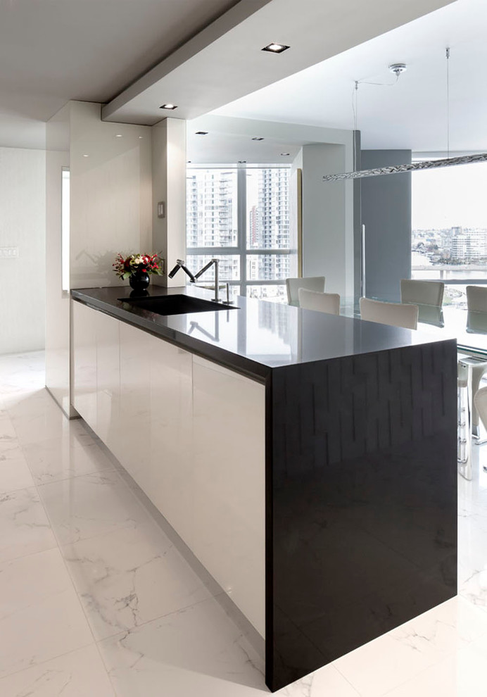 Design ideas for a small modern galley open plan kitchen in Vancouver with flat-panel cabinets, engineered stone countertops, black splashback, an island, a submerged sink, beige cabinets, glass sheet splashback, stainless steel appliances, marble flooring and white floors.