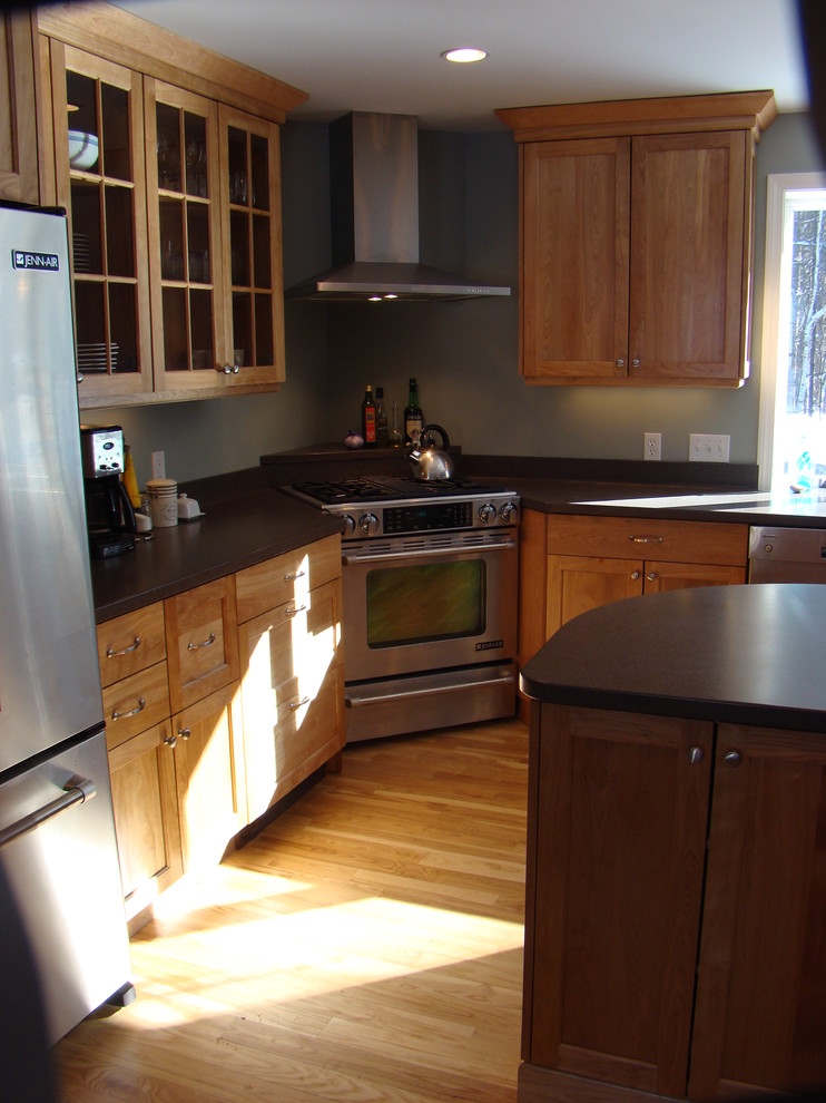 Example of a large trendy l-shaped medium tone wood floor eat-in kitchen design in Portland Maine with an integrated sink, shaker cabinets, medium tone wood cabinets, solid surface countertops, brown backsplash, stainless steel appliances and an island