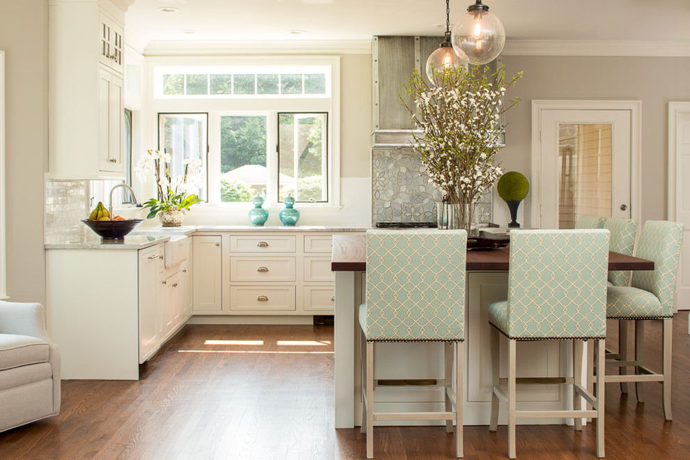 Photo of a classic l-shaped kitchen in Portland Maine with a belfast sink, shaker cabinets, white cabinets, marble worktops, grey splashback, medium hardwood flooring and an island.