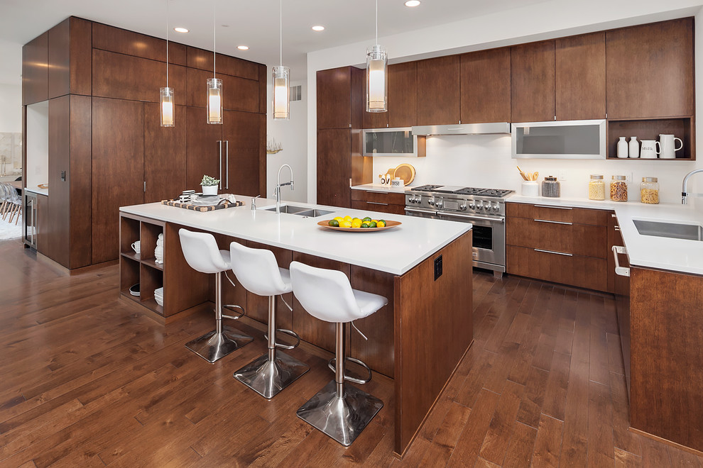 Immagine di un cucina con isola centrale design con lavello sottopiano, ante lisce, ante in legno scuro, paraspruzzi bianco, pavimento in legno massello medio e elettrodomestici da incasso