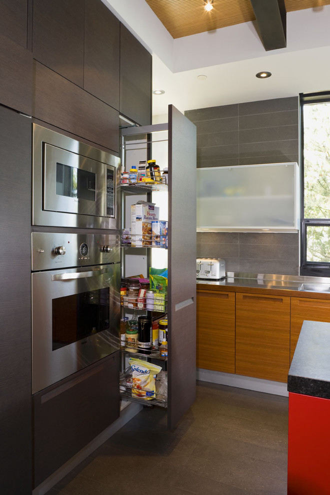 This is an example of a modern galley kitchen/diner in Seattle with flat-panel cabinets, dark wood cabinets, stainless steel worktops, grey splashback, porcelain splashback and stainless steel appliances.