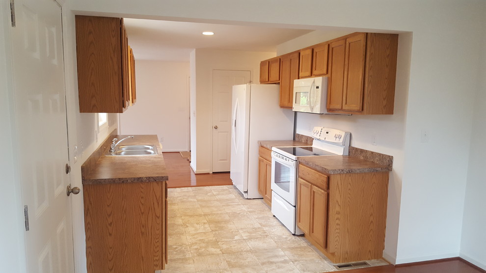 Example of a small classic galley vinyl floor eat-in kitchen design in DC Metro with a double-bowl sink, recessed-panel cabinets, medium tone wood cabinets, laminate countertops, white appliances and no island