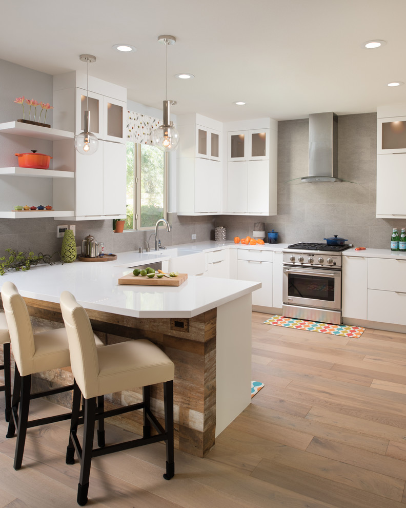 Design ideas for a medium sized traditional u-shaped kitchen in San Diego with a belfast sink, white cabinets, grey splashback, stainless steel appliances, light hardwood flooring, a breakfast bar and flat-panel cabinets.