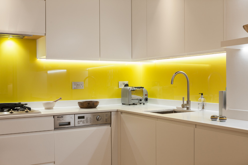 ロンドンにあるラグジュアリーな中くらいなエクレクティックスタイルのおしゃれなキッチン (アンダーカウンターシンク、フラットパネル扉のキャビネット、白いキャビネット、珪岩カウンター、黄色いキッチンパネル、ガラス板のキッチンパネル、シルバーの調理設備、淡色無垢フローリング、アイランドなし) の写真