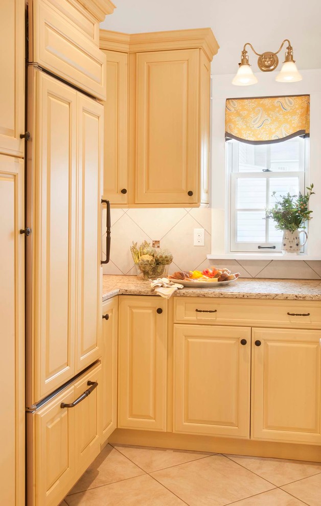 Inspiration for a mid-sized timeless porcelain tile eat-in kitchen remodel in Philadelphia with an undermount sink, raised-panel cabinets, yellow cabinets, granite countertops, beige backsplash, porcelain backsplash, paneled appliances and an island