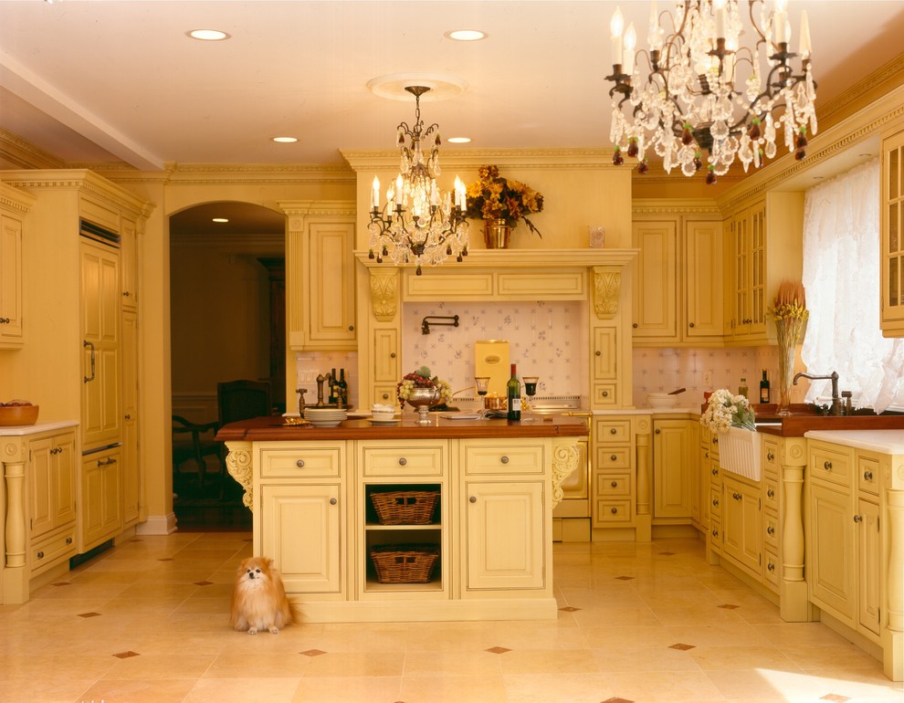 Eat-in kitchen - mid-sized traditional u-shaped limestone floor eat-in kitchen idea in Newark with a farmhouse sink, beaded inset cabinets, yellow cabinets, wood countertops, white backsplash, ceramic backsplash and an island