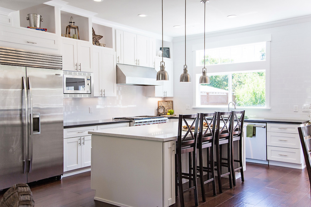 Inspiration for a medium sized l-shaped open plan kitchen in San Francisco with shaker cabinets, white cabinets, quartz worktops, white splashback, porcelain splashback, stainless steel appliances, dark hardwood flooring, an island, brown floors and white worktops.