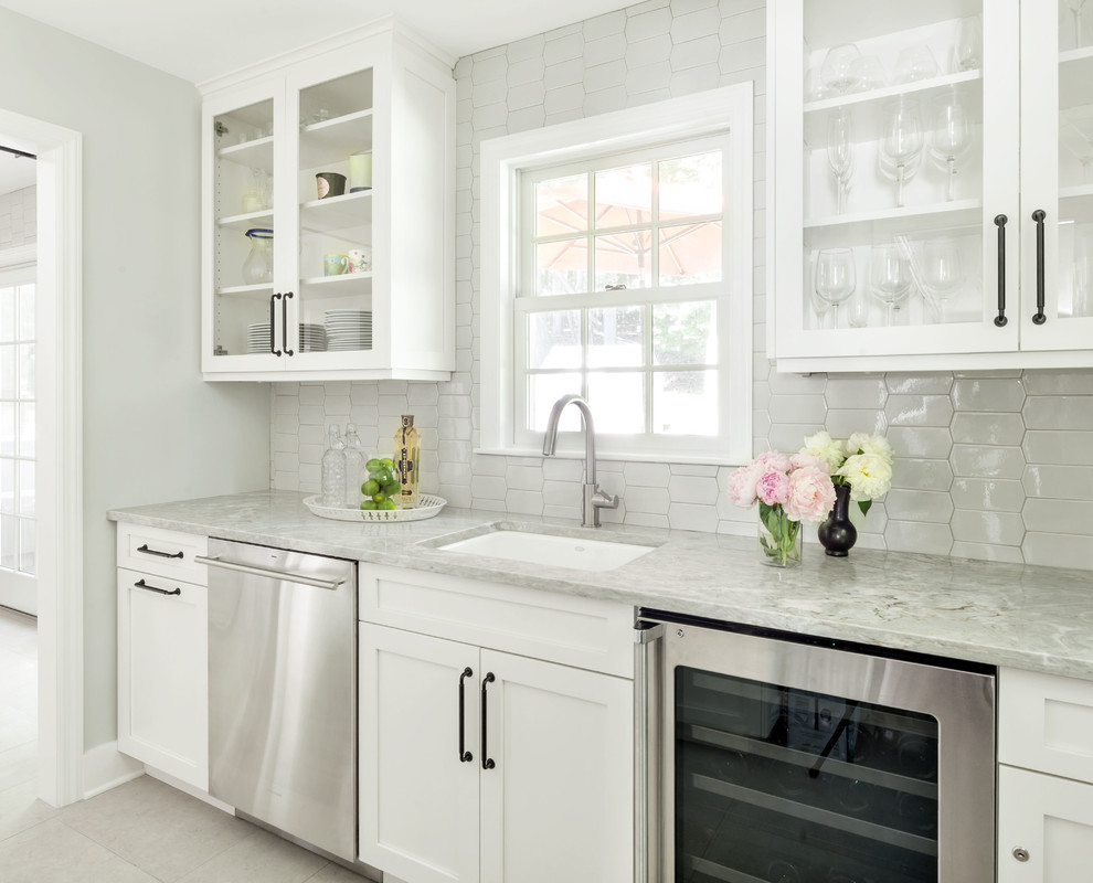 Enclosed kitchen - mid-sized transitional l-shaped porcelain tile and beige floor enclosed kitchen idea in New York with a farmhouse sink, shaker cabinets, white cabinets, quartzite countertops, gray backsplash, ceramic backsplash, stainless steel appliances, an island and gray countertops