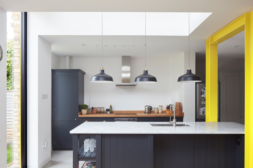 ロンドンにある北欧スタイルのおしゃれなアイランドキッチン (アンダーカウンターシンク、シェーカースタイル扉のキャビネット、黒いキャビネット、木材カウンター、グレーの床) の写真