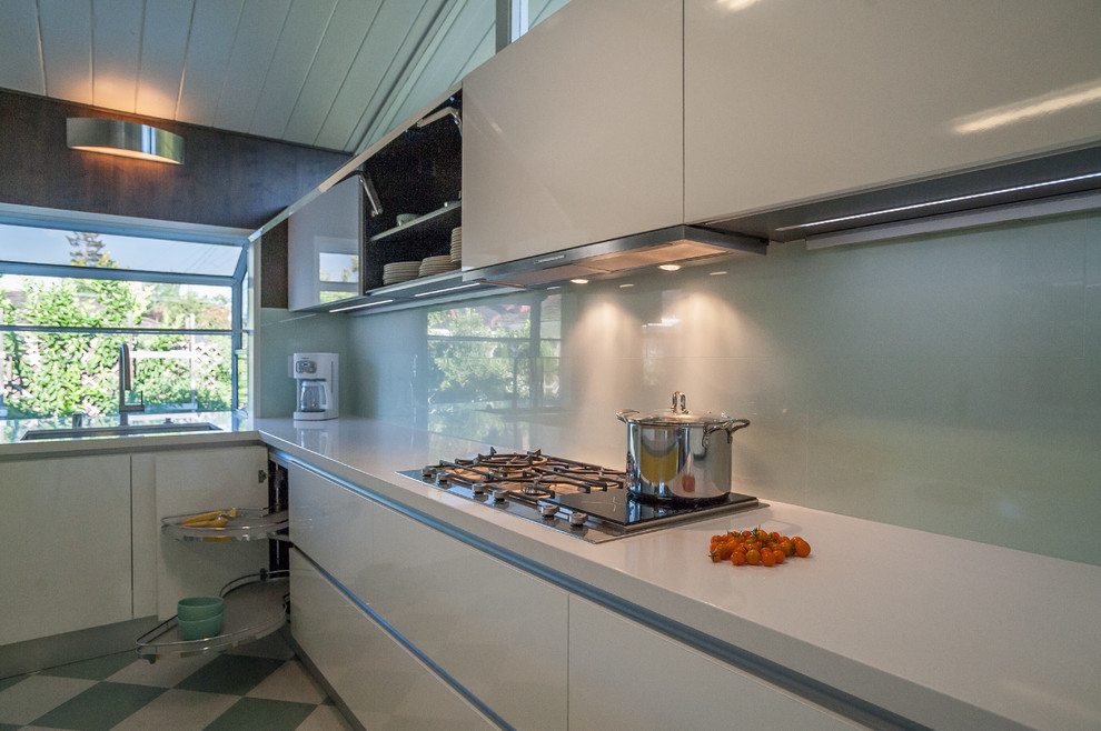 Mid-sized trendy galley linoleum floor eat-in kitchen photo in San Francisco with flat-panel cabinets, white cabinets, stainless steel appliances, an island, a drop-in sink, solid surface countertops, gray backsplash and stone slab backsplash