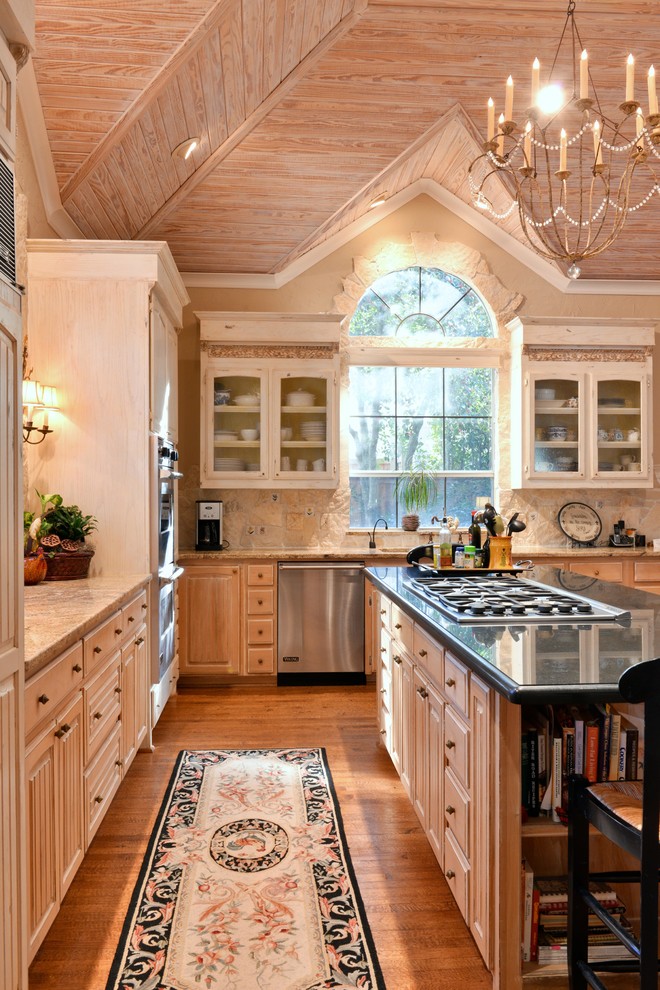 Cette image montre une cuisine chalet en L et bois clair avec un plan de travail en granite, un placard avec porte à panneau surélevé, une crédence beige, un électroménager en acier inoxydable, un sol en bois brun, îlot et une crédence en pierre calcaire.