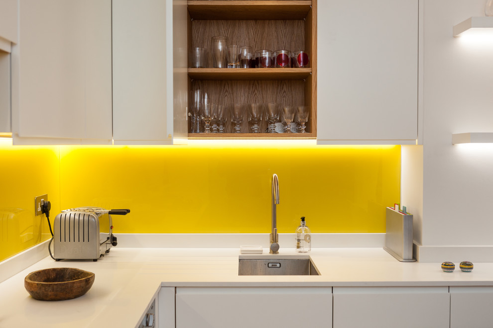 Open concept kitchen - mid-sized eclectic l-shaped light wood floor open concept kitchen idea in London with an undermount sink, flat-panel cabinets, white cabinets, quartzite countertops, yellow backsplash, glass sheet backsplash, stainless steel appliances and no island