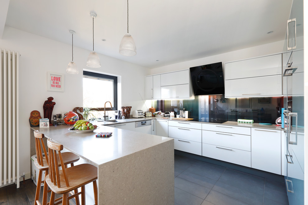 Inspiration for a medium sized modern u-shaped open plan kitchen in Sussex with a built-in sink, flat-panel cabinets, white cabinets, composite countertops, multi-coloured splashback, glass sheet splashback, black appliances, ceramic flooring and a breakfast bar.