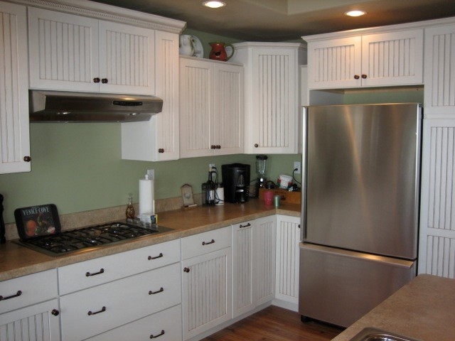 Exempel på ett mellanstort amerikanskt linjärt kök och matrum, med en undermonterad diskho, luckor med infälld panel, vita skåp, rostfria vitvaror, ljust trägolv, en köksö, granitbänkskiva, beige stänkskydd och stänkskydd i sten