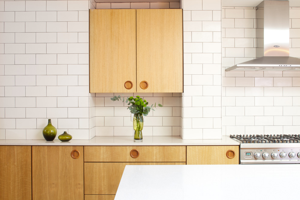 Foto de cocina moderna grande abierta con armarios con paneles lisos, puertas de armario de madera clara, salpicadero blanco, salpicadero de azulejos de cerámica, electrodomésticos con paneles y una isla