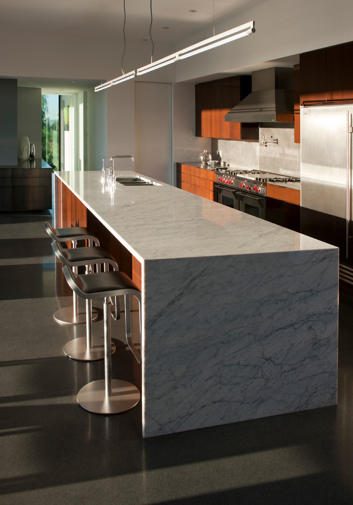 Foto di una cucina moderna di medie dimensioni con lavello sottopiano, ante lisce, ante in legno bruno, top in marmo, paraspruzzi grigio, elettrodomestici in acciaio inossidabile e pavimento in cemento