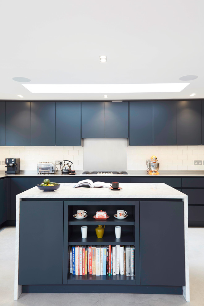 This is an example of a large contemporary l-shaped open plan kitchen in London with a double-bowl sink, flat-panel cabinets, blue cabinets, stainless steel worktops, white splashback, metro tiled splashback, integrated appliances, an island and grey floors.