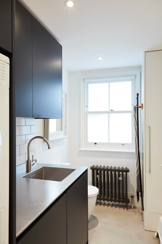 ロンドンにある高級な広いコンテンポラリースタイルのおしゃれなキッチン (ダブルシンク、フラットパネル扉のキャビネット、青いキャビネット、ステンレスカウンター、白いキッチンパネル、サブウェイタイルのキッチンパネル、パネルと同色の調理設備、グレーの床) の写真