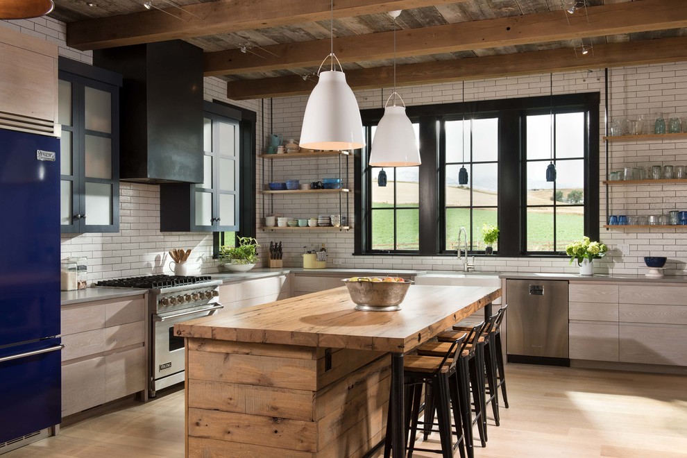 Example of a farmhouse l-shaped light wood floor and beige floor kitchen design in Other with a farmhouse sink, open cabinets, light wood cabinets, wood countertops, white backsplash, subway tile backsplash, colored appliances and an island