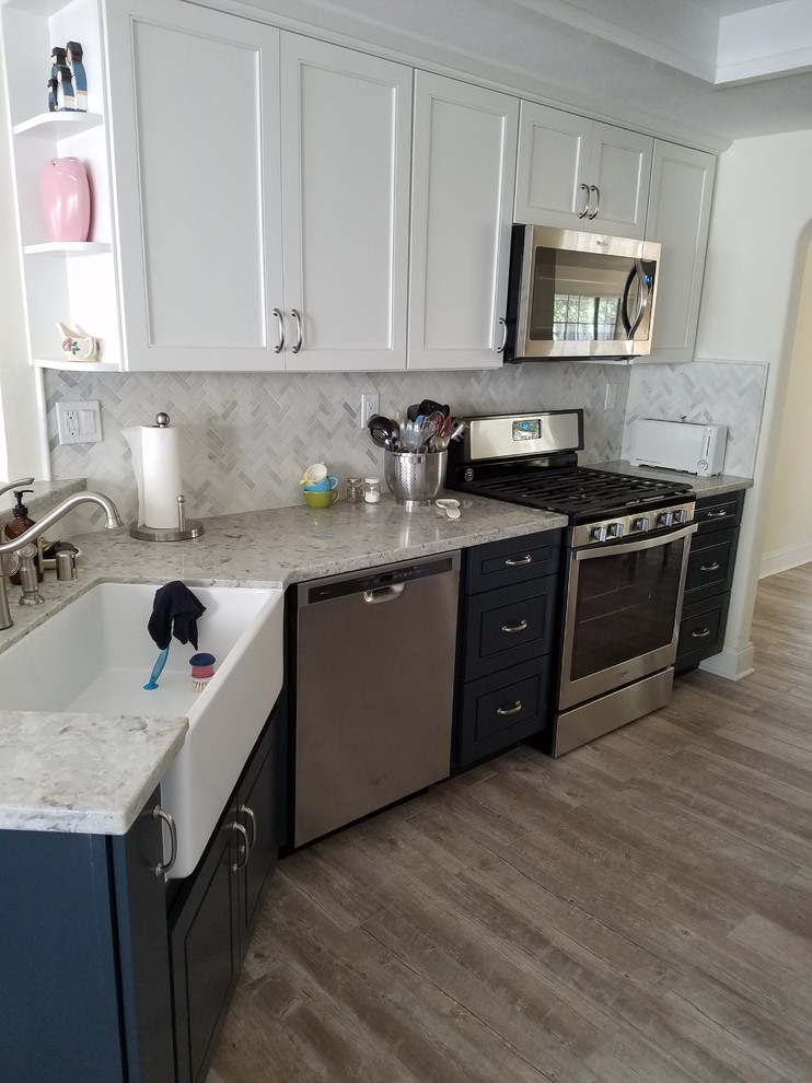 Inredning av ett lantligt stort grå grått kök, med en rustik diskho, luckor med upphöjd panel, blå skåp, granitbänkskiva, vitt stänkskydd, stänkskydd i stenkakel, rostfria vitvaror, laminatgolv och brunt golv