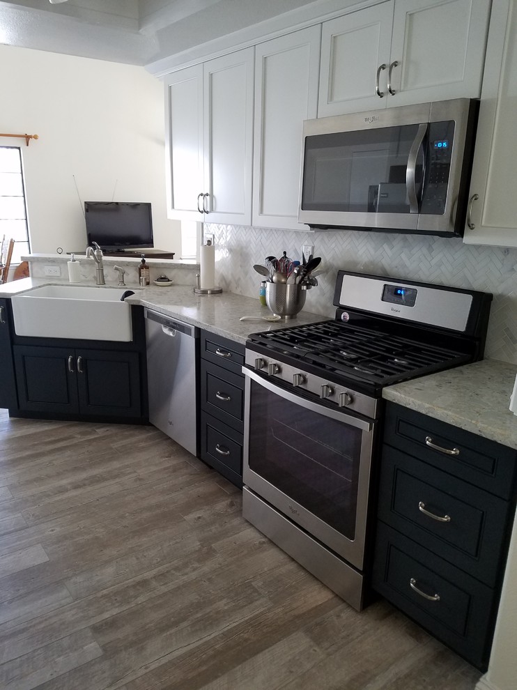 Bild på ett stort lantligt grå grått kök, med en rustik diskho, luckor med upphöjd panel, blå skåp, granitbänkskiva, vitt stänkskydd, stänkskydd i stenkakel, rostfria vitvaror, laminatgolv och brunt golv