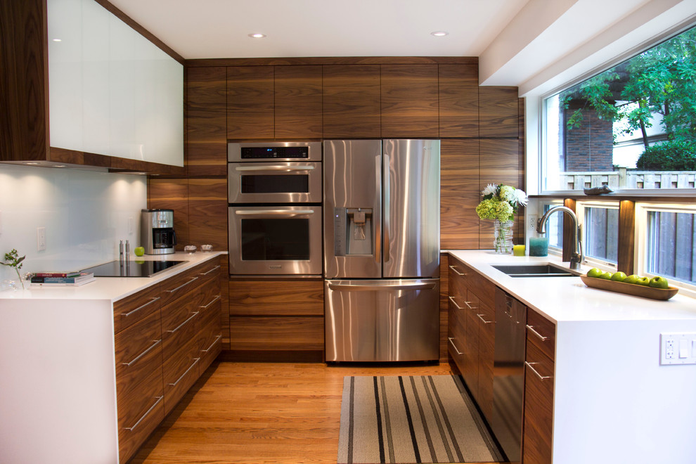 Midcentury u-shaped kitchen in Toronto with a double-bowl sink, flat-panel cabinets, dark wood cabinets, white splashback, glass sheet splashback and stainless steel appliances.