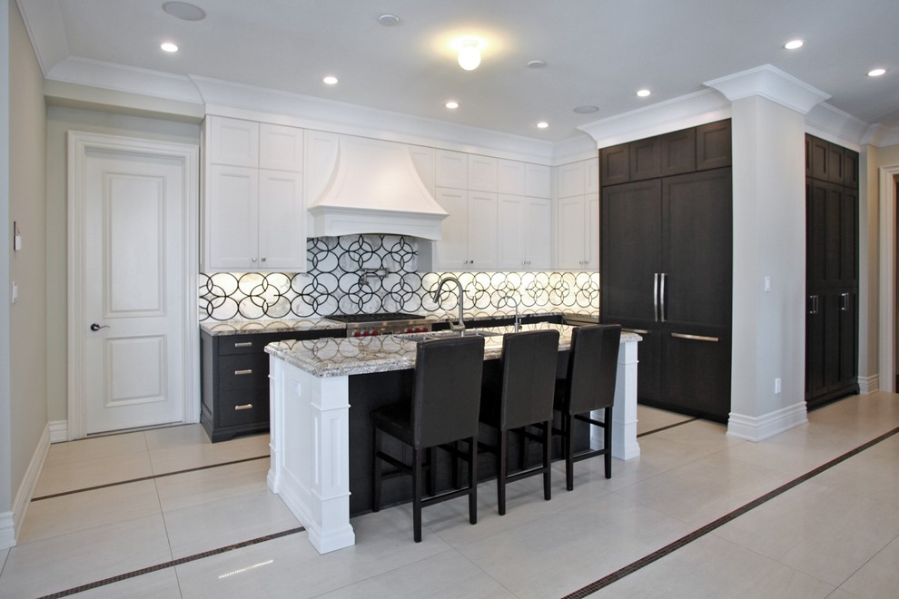 Klassisk inredning av ett stort linjärt kök och matrum, med en dubbel diskho, vita skåp, granitbänkskiva, grått stänkskydd, rostfria vitvaror och en köksö