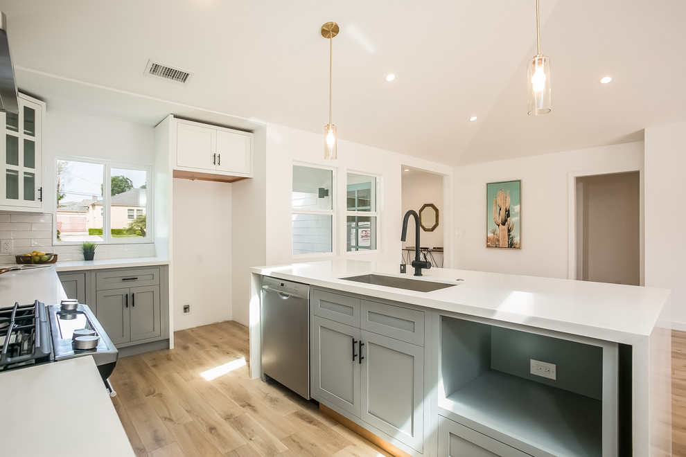 Example of a cottage l-shaped light wood floor and brown floor eat-in kitchen design in Los Angeles with an undermount sink, shaker cabinets, white cabinets, quartz countertops, white backsplash, marble backsplash, stainless steel appliances and an island