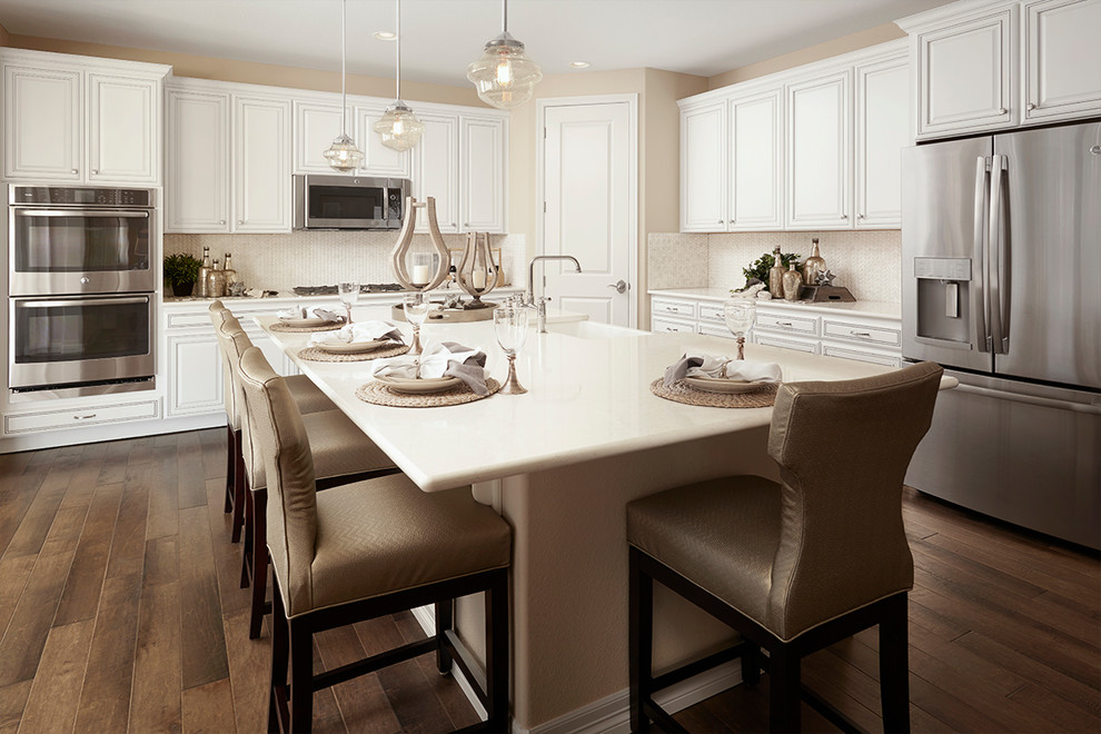 Diseño de cocina clásica renovada con puertas de armario blancas, salpicadero blanco, electrodomésticos de acero inoxidable, una isla, suelo marrón y encimeras blancas